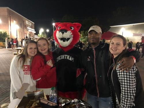 {Four people stand with Pouncer at an evening alumni event}